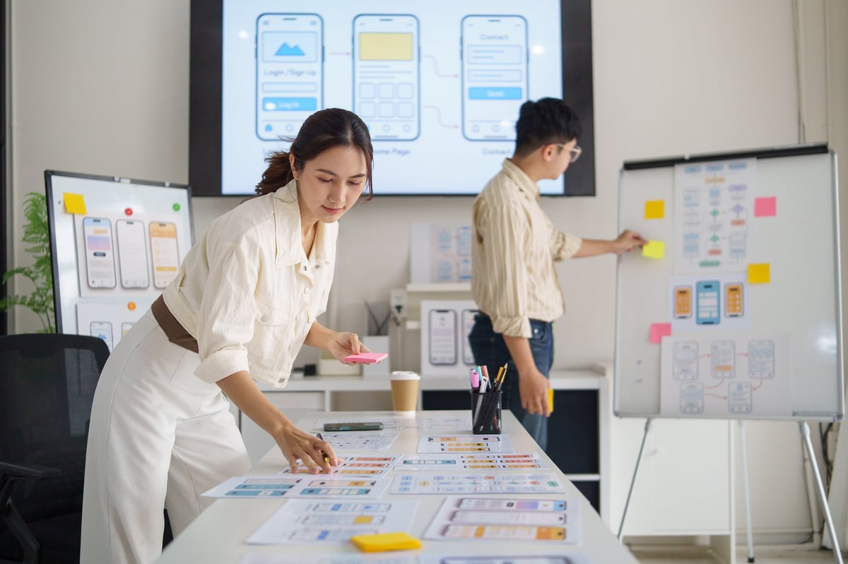 UX designer writing notes on sticky paper while planning mobile app interface.